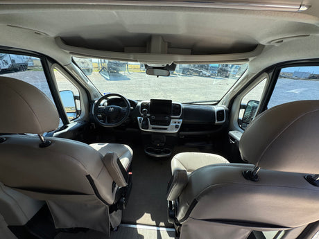 Spacious RV rental cockpit: front seats, modern dashboard, and an outdoor view of other RVs in a lot.