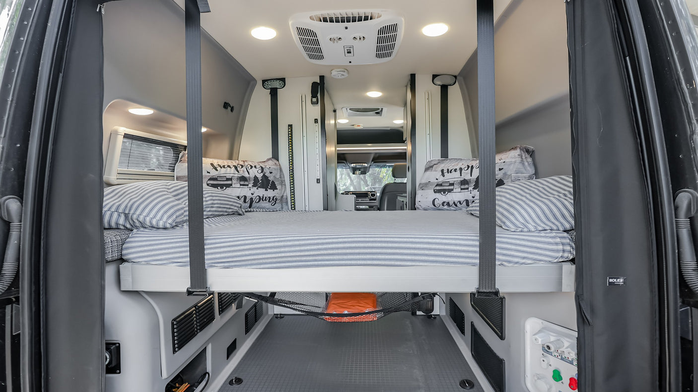 This RV rental's elevated bed features striped bedding & ample under-bed storage. Bright interior for your camping journey.