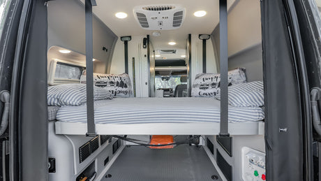 This RV rental's elevated bed features striped bedding & ample under-bed storage. Bright interior for your camping journey.