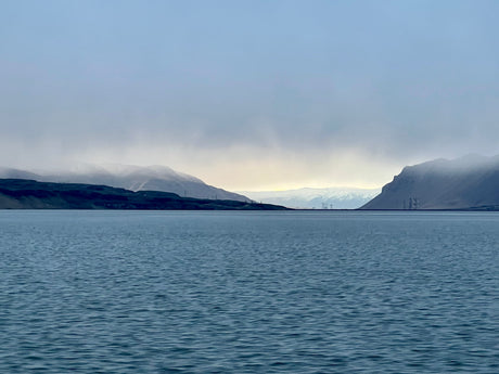 Serene fjord framed by misty mountains under a pale sky. Discover with an RV rental.