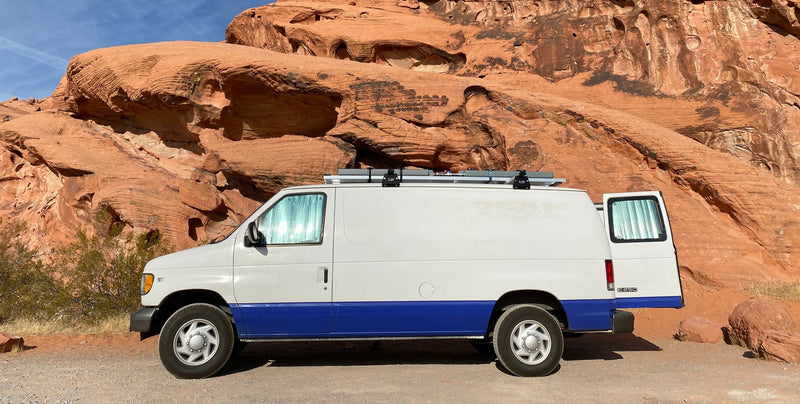 This white and blue van (REAL Racing Services), resembling an RV rental, is parked against vibrant red rock cliffs, perfect for travel. — photo 6