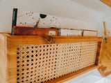 Stylish wooden shelf with books & woven cane detail in an RV rental. Perfect storage for organized travels.