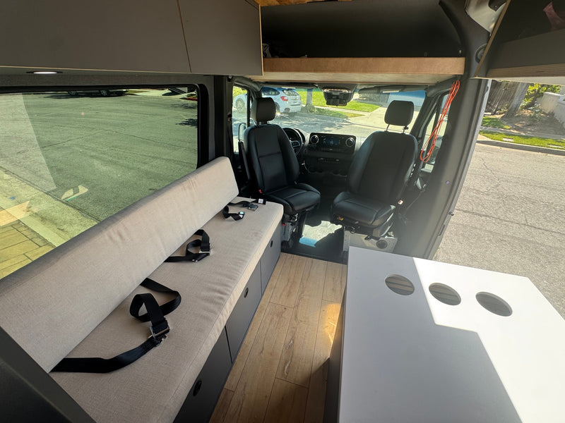 Bright rv rental interior with a bench seat and seatbelts, wood floor, swivel front seats, overhead storage, and a white table. — photo 16