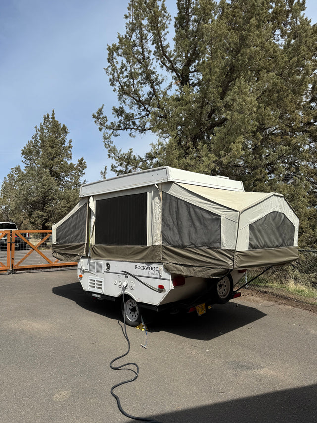 Pop-up RV rental: A Rockwood Freedom camper extended on asphalt with power cord, ready for your camping travel.