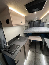Interior of a modern rv rental featuring a compact kitchen with induction cooktop, bed area, and integrated storage.