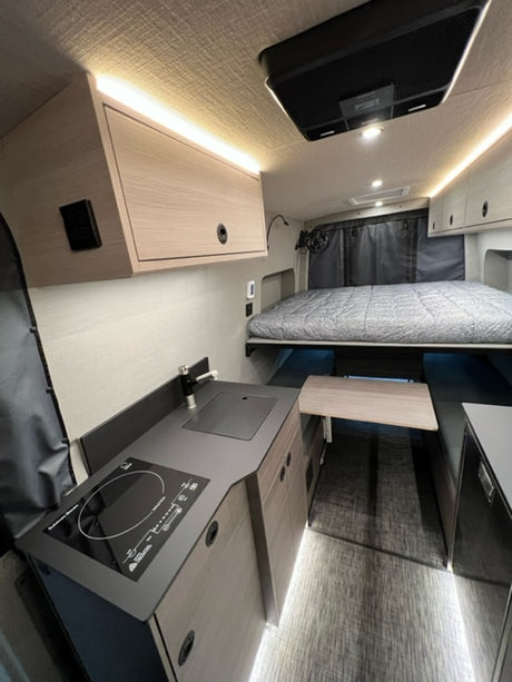 Interior of a modern rv rental featuring a compact kitchen with induction cooktop, bed area, and integrated storage.