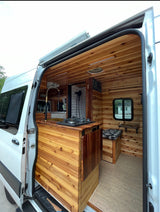 This cozy, cedar-paneled camper van, perfect for rv rental, features a kitchen, shower, and seating. Ideal for mobile living.