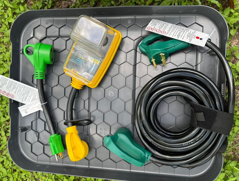 RV rental power essentials: 30A circuit analyzer, coiled black power cord, and green/yellow adapters. On a gray tray. — photo 6