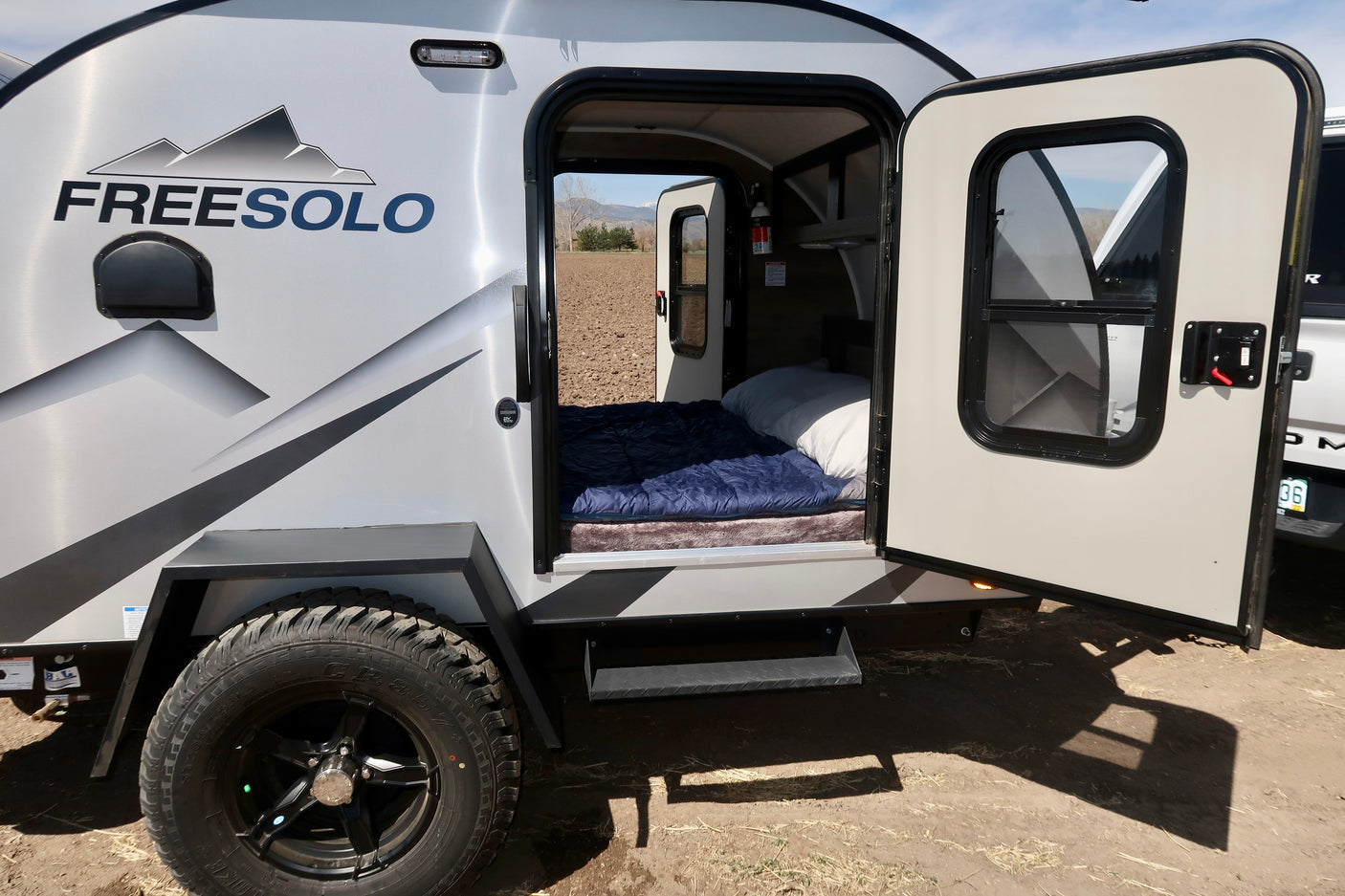 Cozy Freesolo small travel trailer with open door & bed, ideal for an RV rental camping trip & outdoor adventure.