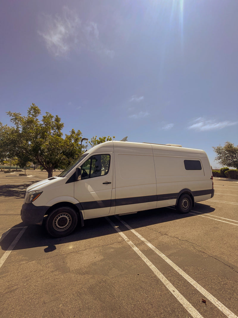 A white Sprinter-style camper van, ideal for an RV rental, parked in a sunny lot under a clear blue sky. — photo 12