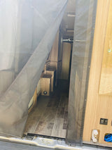 Enter this RV rental! A sturdy mesh screen door protects the interior, showcasing wood-grain flooring and utility controls.