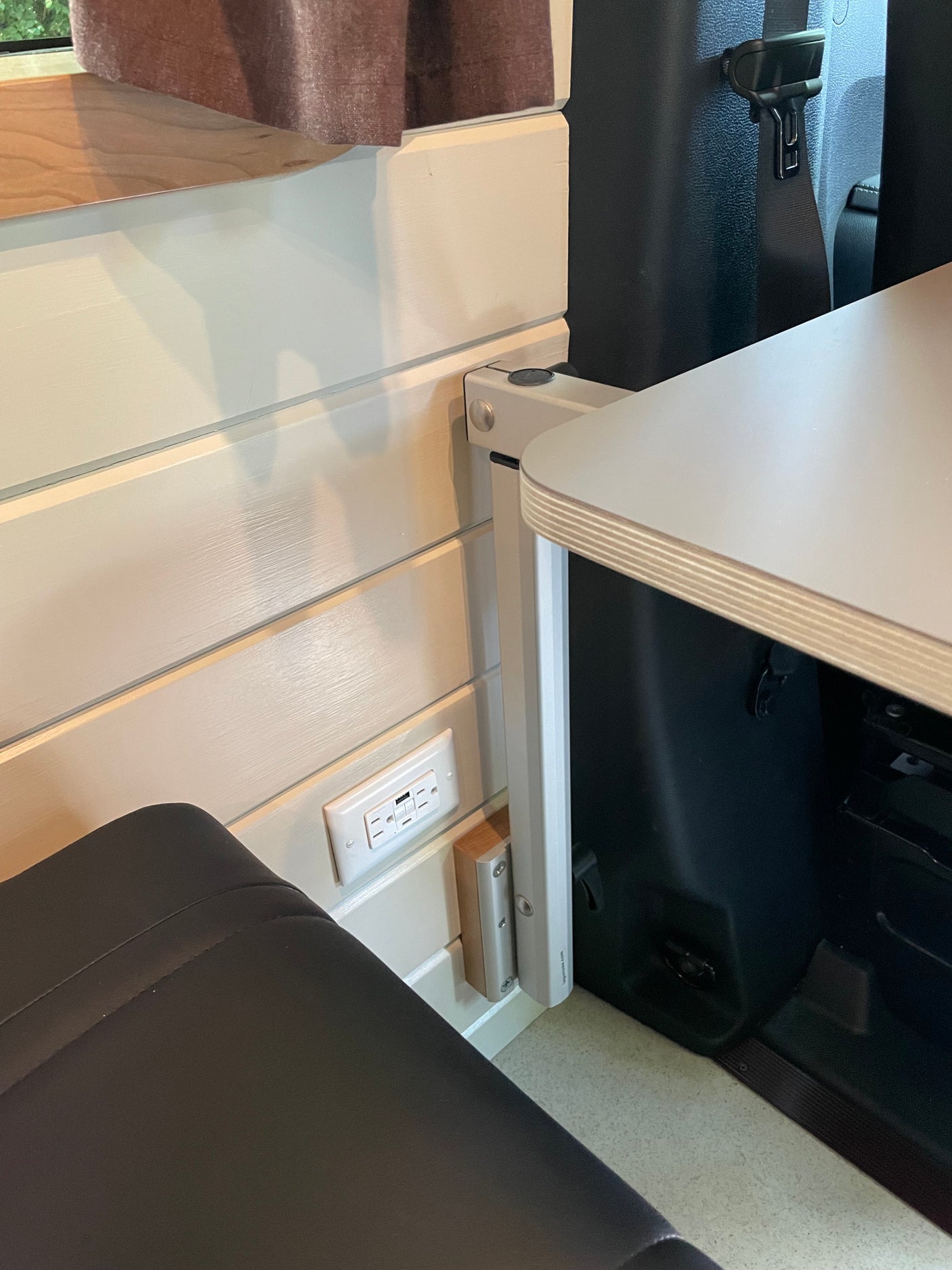 View inside an RV rental, featuring a practical fold-down table, built-in power outlet with USB ports, and a dark upholstered seat.