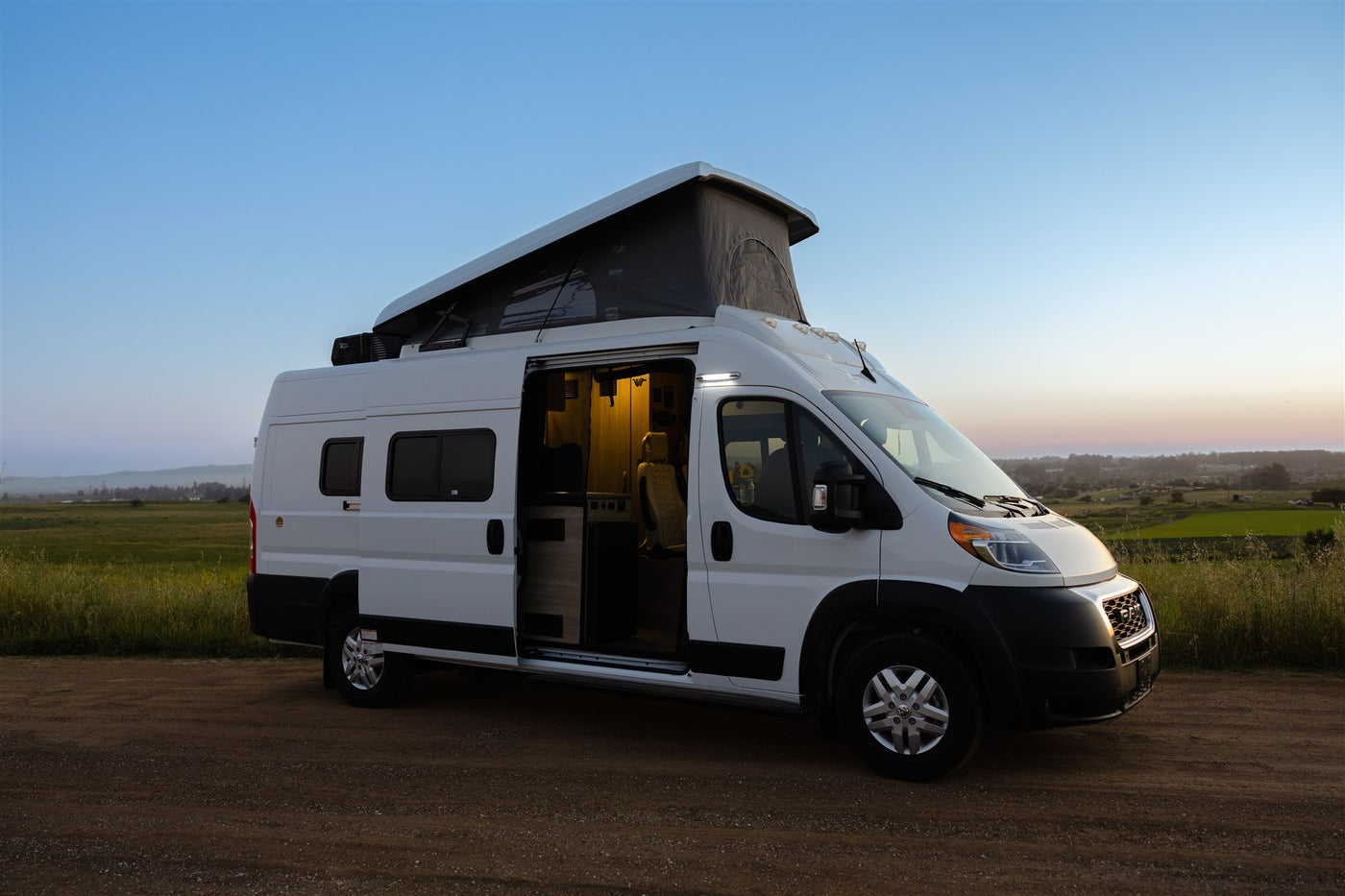  reveals its cozy interior at sunset on a dirt road.|Explore your next RV rental: modern camper van interior with swivel seats — photo 6