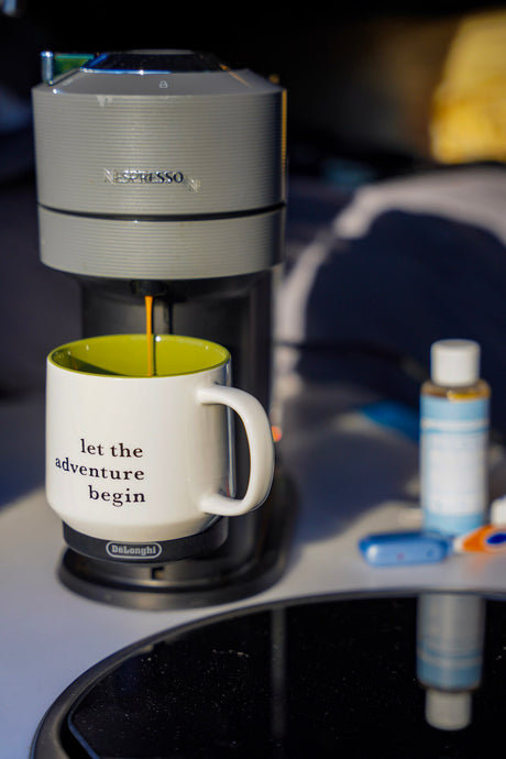 Nespresso coffee brews into a "let the adventure begin" mug inside an RV rental. Perfect start to a road trip.