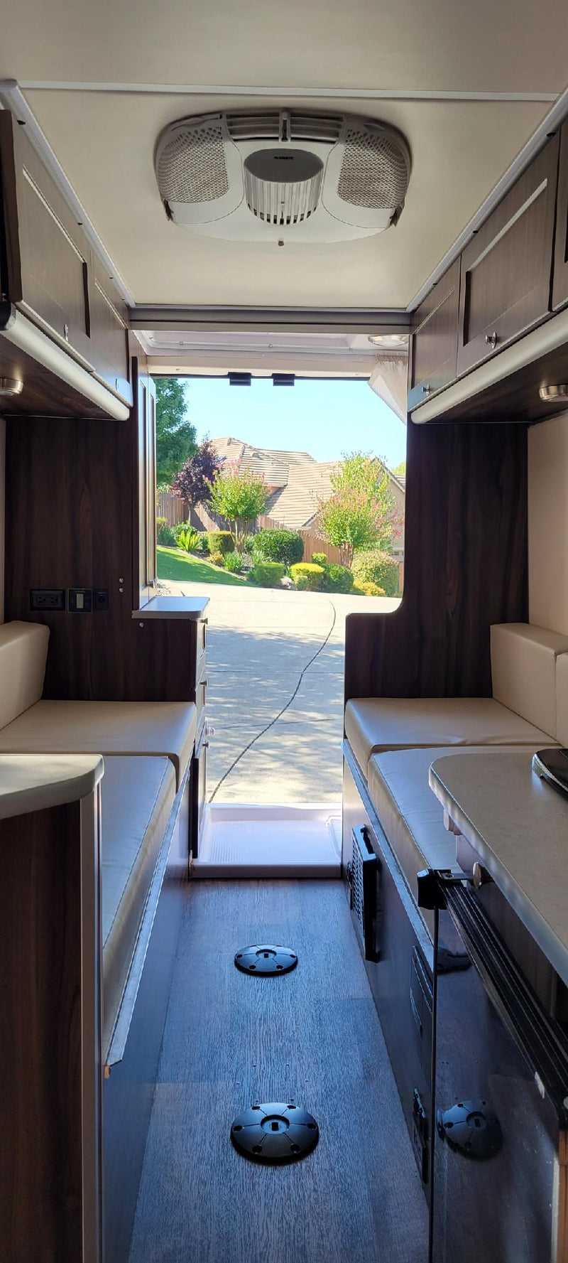 Spacious RV rental interior, looking out the open rear door at a suburban street. Features comfortable seating and a ceiling AC. — photo 9