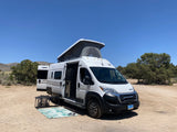 White Winnebago Solis rv rental van with side door open and pop-top extended, set up for desert camping.
