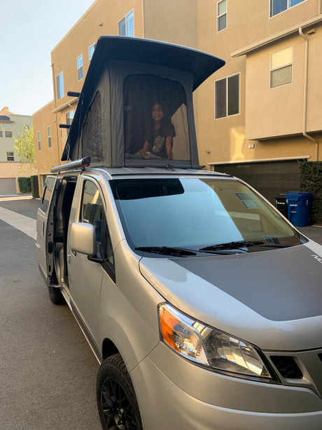 Smiling girl in a silver pop-top camper van, a perfect RV rental for your next adventure.