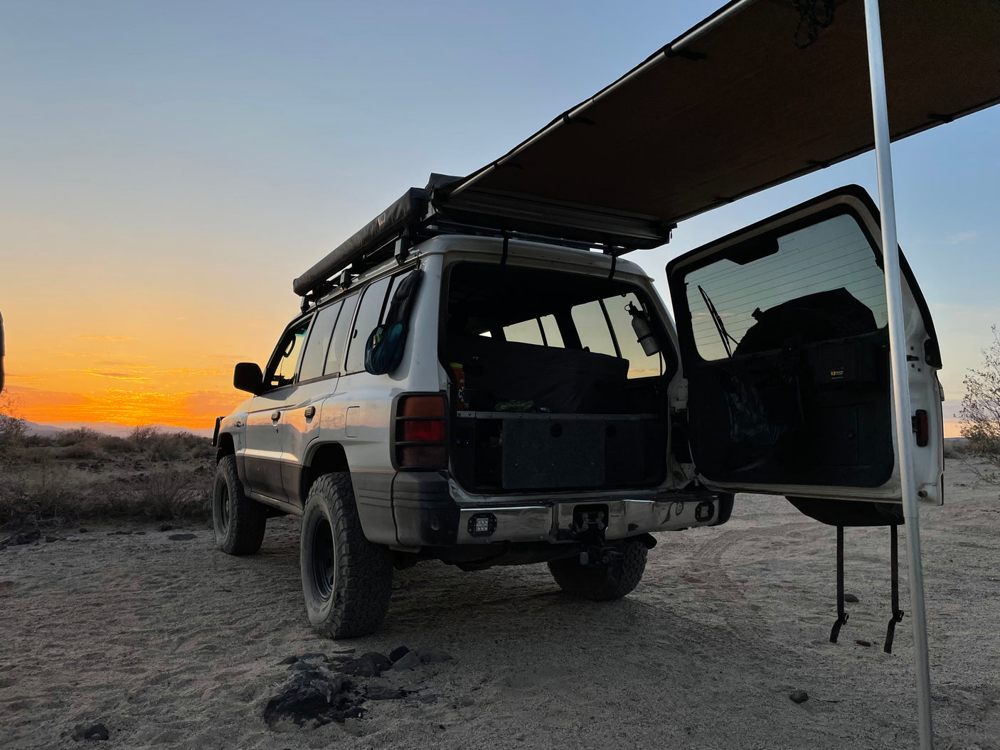 Overland SUV, awning deployed, open rear hatch at desert sunset. Perfect for camping, similar to an RV rental experience!