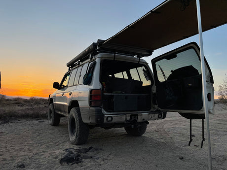 Overland SUV, awning deployed, open rear hatch at desert sunset. Perfect for camping, similar to an RV rental experience!