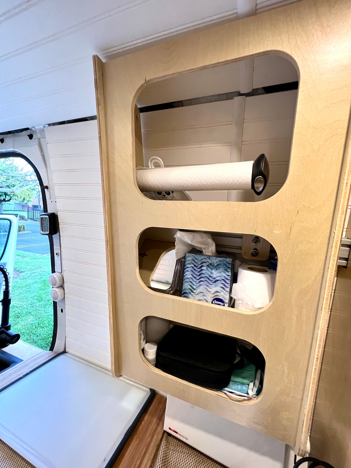 Organized interior of an RV rental. A wooden cabinet features open storage for paper towels, tissues, and toiletries.
