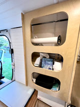 Organized interior of an RV rental. A wooden cabinet features open storage for paper towels, tissues, and toiletries.