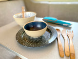 A cozy dining setup inside an RV rental, featuring two bowls, a speckled plate, and wooden utensils on a table.