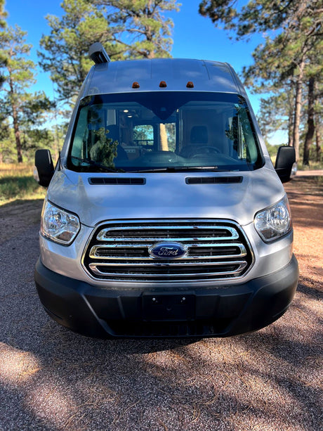 Front view of a silver Ford Transit camper van, ideal rv rental for outdoor adventures, parked on a dirt road.