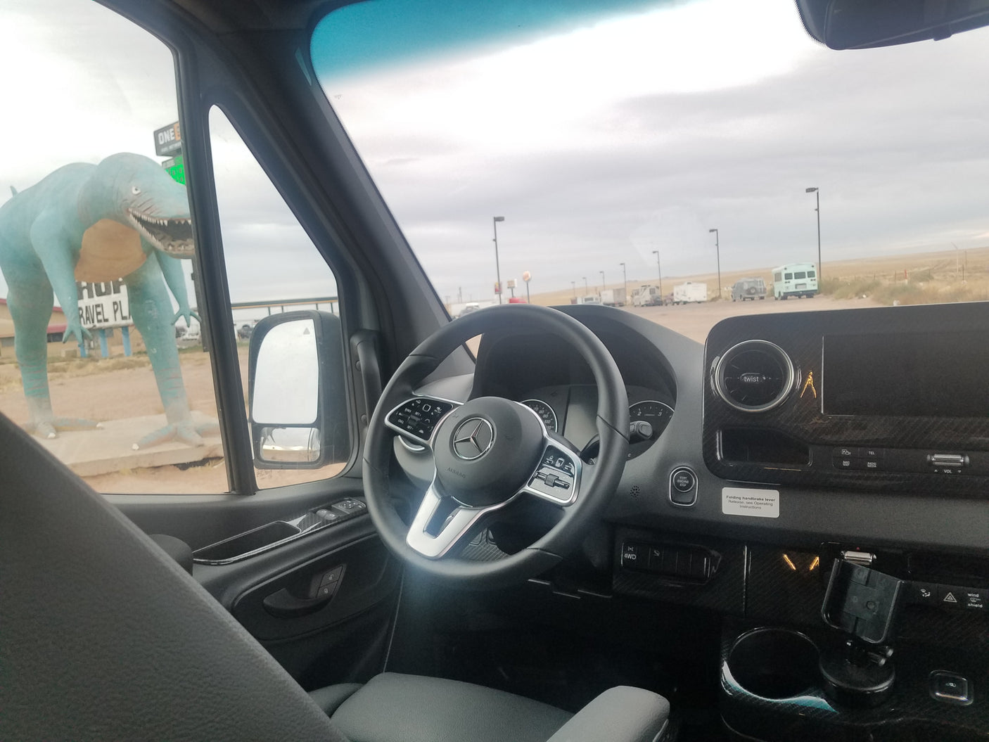 RV rental van interior overlooking a large blue dinosaur statue at a travel plaza with other parked RVs, perfect for travel.