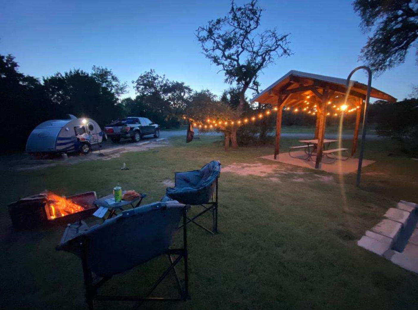 Enjoy an RV rental camping getaway! This cozy site features a teardrop trailer, bright campfire, and string-lit pavilion.
