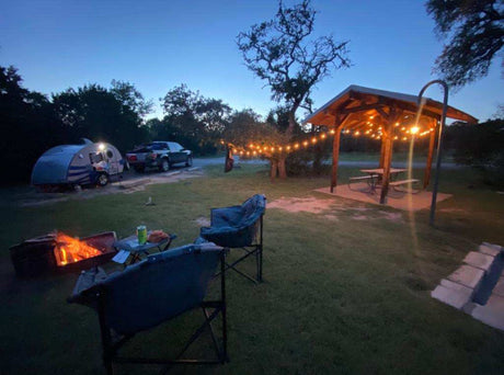 Enjoy an RV rental camping getaway! This cozy site features a teardrop trailer, bright campfire, and string-lit pavilion.