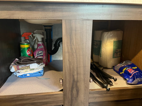 Organized storage in an RV rental under-sink cabinet: cleaning supplies, towels, paper towels, and plastic cutlery.