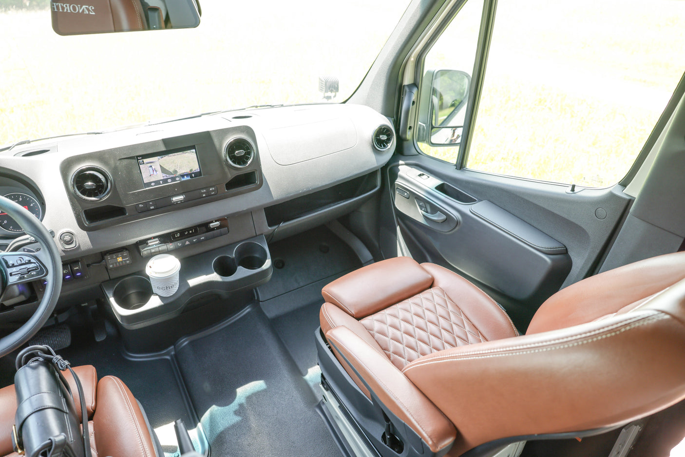 Spacious RV rental cockpit: modern dashboard, large display screen, and comfortable brown leather quilted seats for an enjoyable drive.