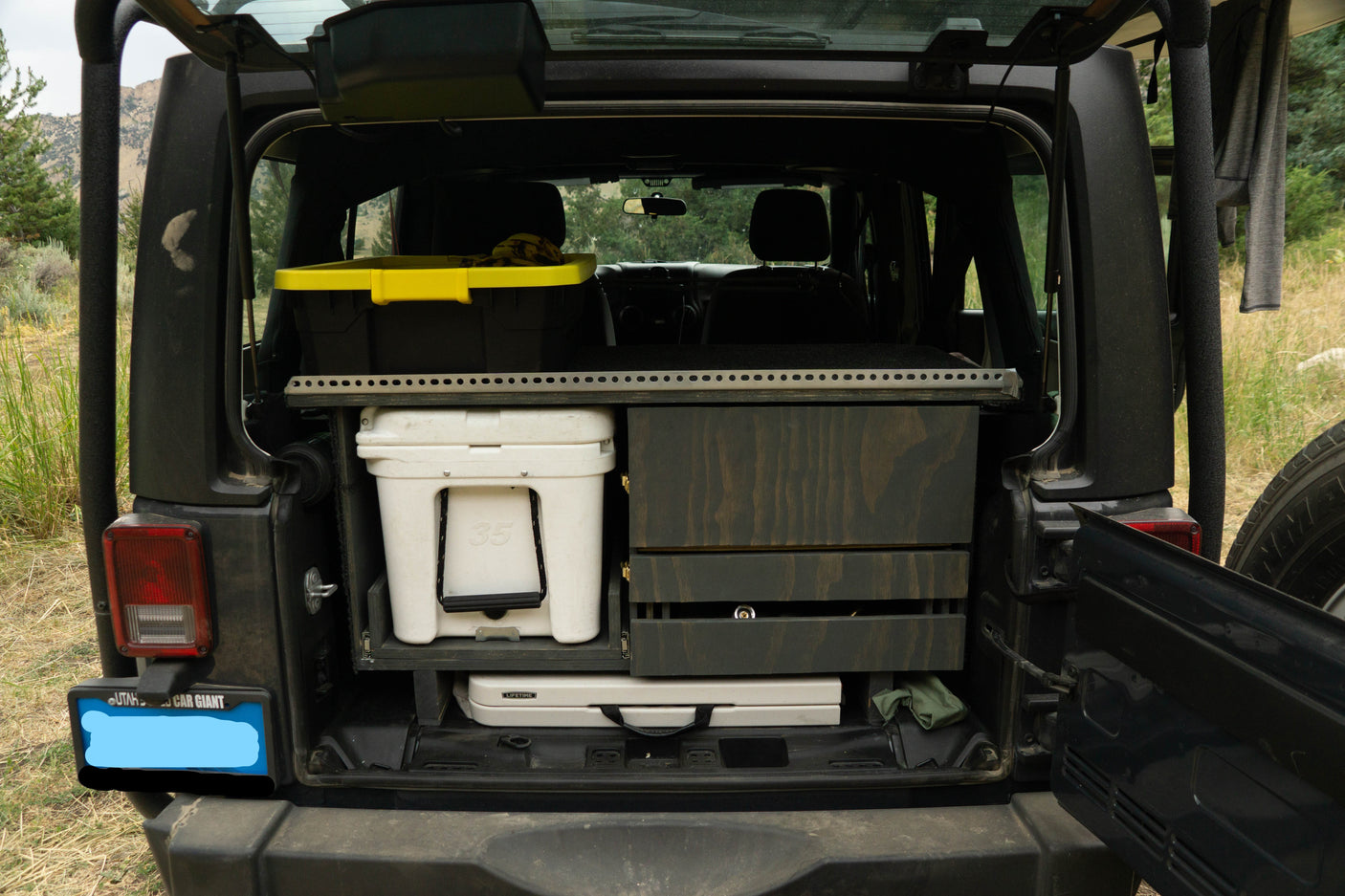 Rear of an SUV with custom camping storage: Yeti cooler, drawers, and bin. Ideal for RV rental adventures or overlanding.