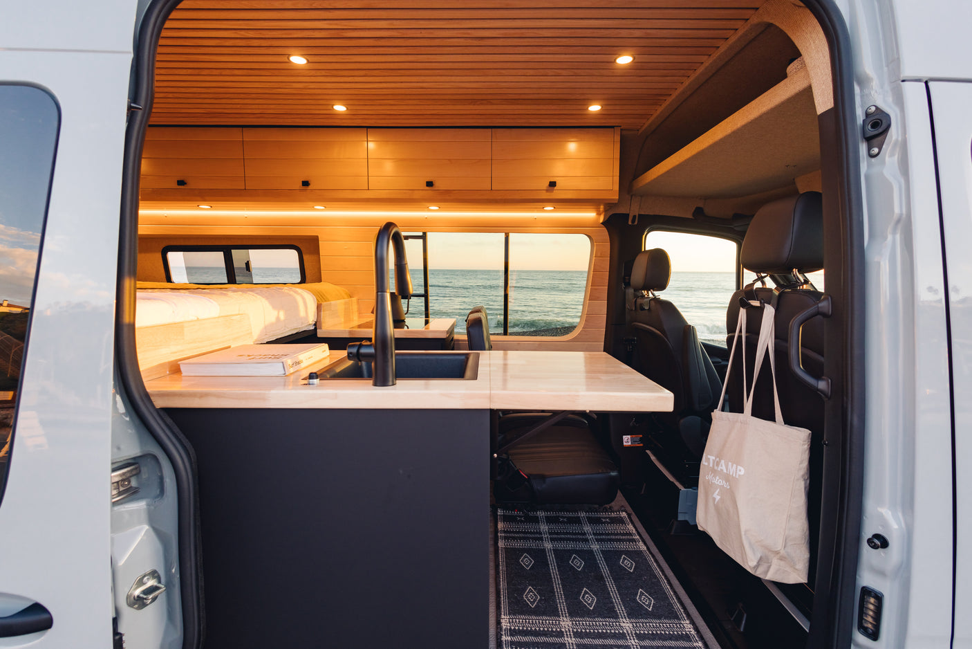 Custom RV rental interior: wood-paneled ceiling, modern kitchen, cozy bed & ocean view. Ideal for stylish road trips.