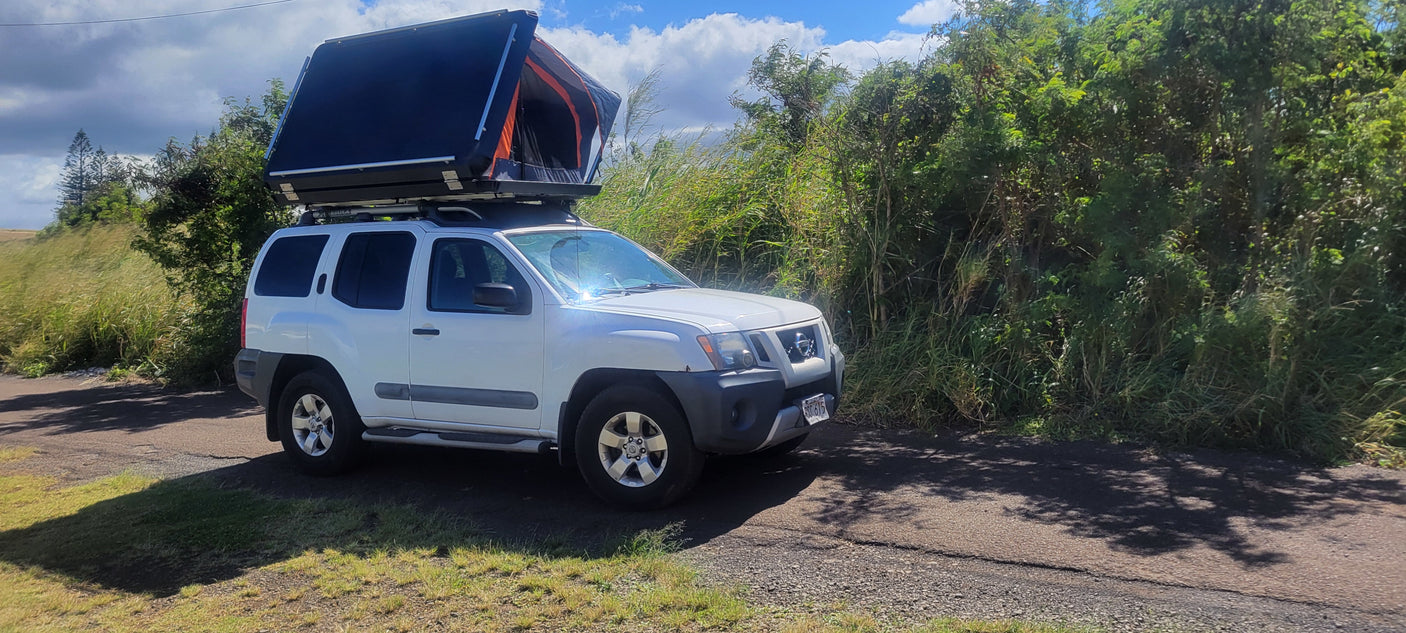 White Nissan Xterra SUV with deployed rooftop tent. Perfect for your RV rental, offering outdoor adventure & camping.