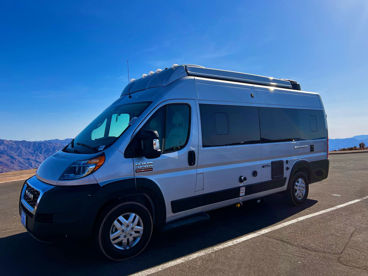 Silver Ram ProMaster camper van, perfect for RV rental, shines under a clear sky with majestic mountains in the background. — photo 18