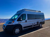 Silver Ram ProMaster camper van, perfect for RV rental, shines under a clear sky with majestic mountains in the background.