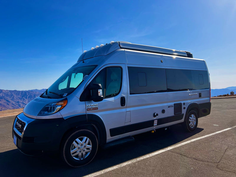 Silver Ram ProMaster camper van, perfect for RV rental, shines under a clear sky with majestic mountains in the background. — photo 18