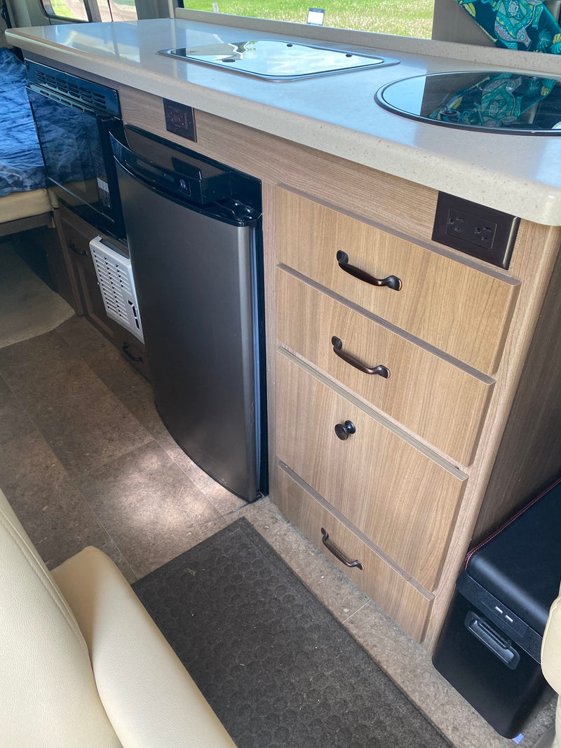 RV rental kitchen: light countertop, built-in stove/sink, microwave, compact fridge, & wood-look drawers. — photo 8