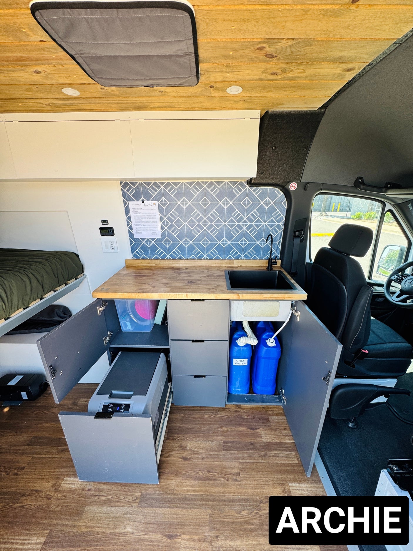 This RV rental's modern camper van interior features a kitchen with sink & fridge, clever storage, and a cozy bed for van life.