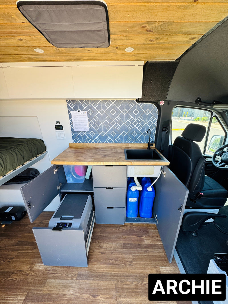 This RV rental's modern camper van interior features a kitchen with sink & fridge, clever storage, and a cozy bed for van life. — photo 4