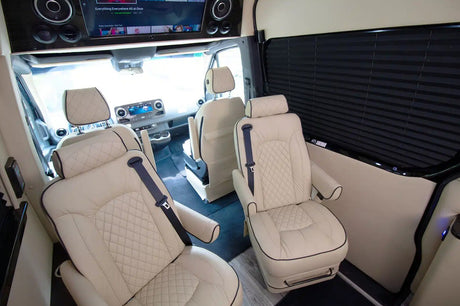 Spacious RV rental interior with luxurious cream quilted leather passenger seats, entertainment screen, and window blinds.
