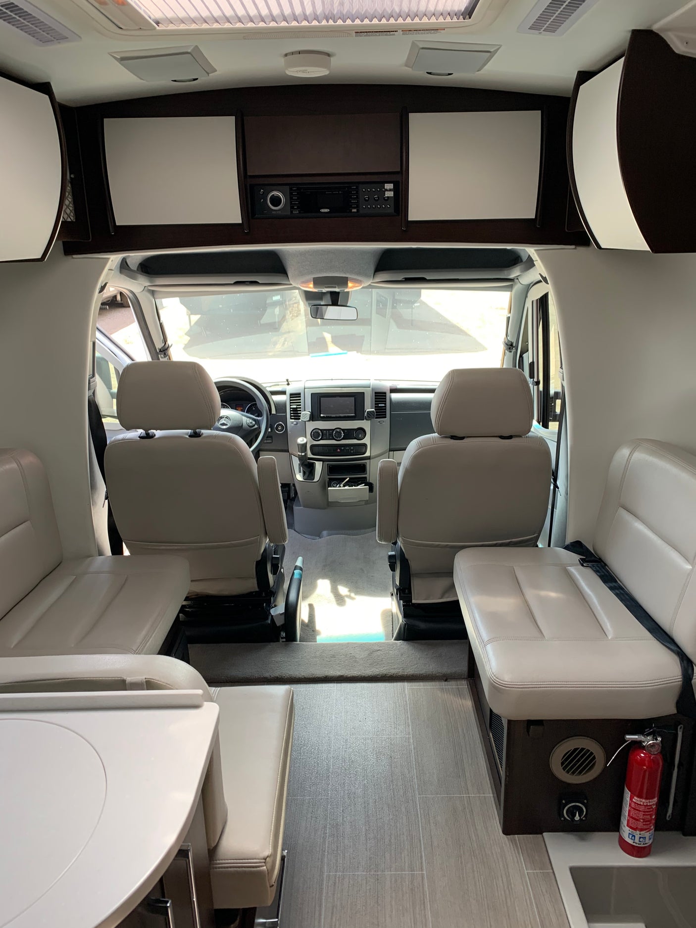 RV rental interior: Looking towards the cockpit from the rear living area, showing driver/passenger seats, table, and storage.
