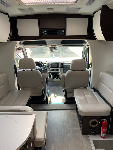 RV rental interior: Looking towards the cockpit from the rear living area, showing driver/passenger seats, table, and storage.