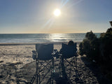 Two chairs face the glowing sun over the ocean on a sandy beach, ideal after an RV rental trip.