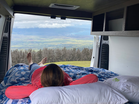 Relaxing in an RV rental: a person enjoys a panoramic valley and ocean view from bed inside a camper van. Ideal travel.