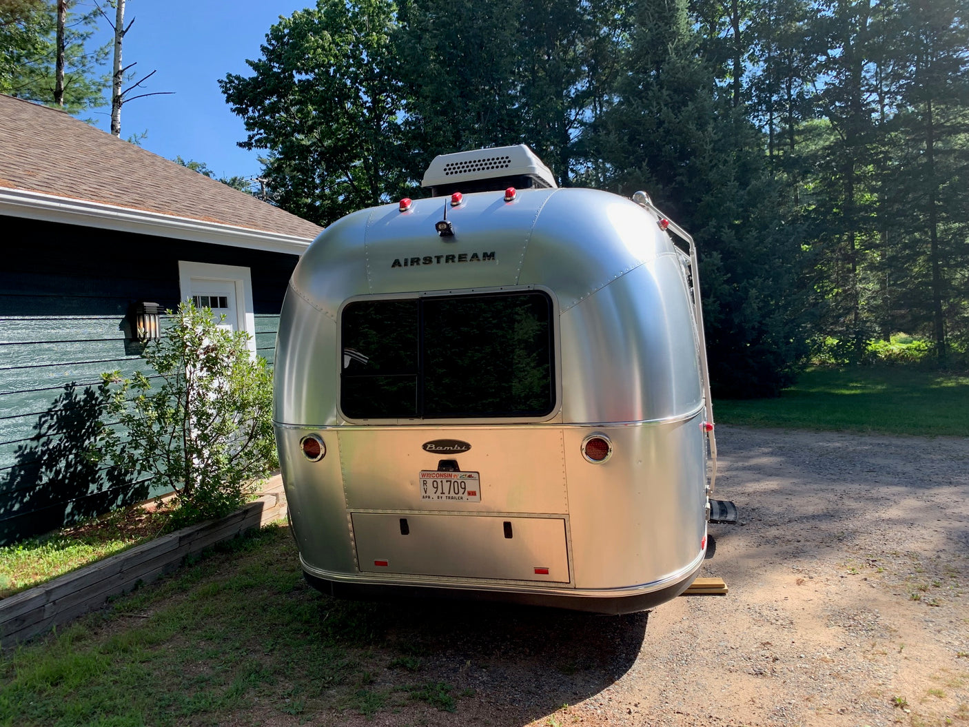 Airstream Bambi travel trailer, often available for rv rental, parked by a house amidst green trees.