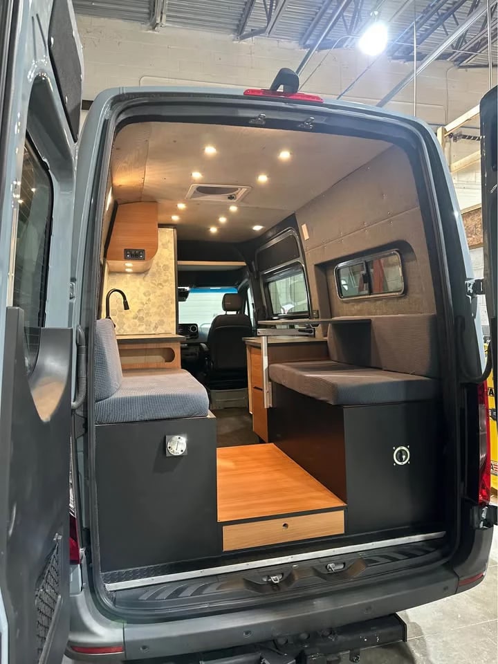 Interior of a modern camper van conversion, featuring a compact kitchen, comfy seating/bed, and ample storage. Perfect for your rv rental adventure.