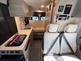 Explore this Winnebago RV rental interior: featuring a kitchenette, rear seating, and a detailed control panel.