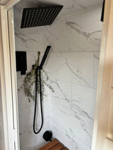 Modern RV rental shower: black fixtures, elegant marble-look tiles, and dried eucalyptus for a refreshing experience.